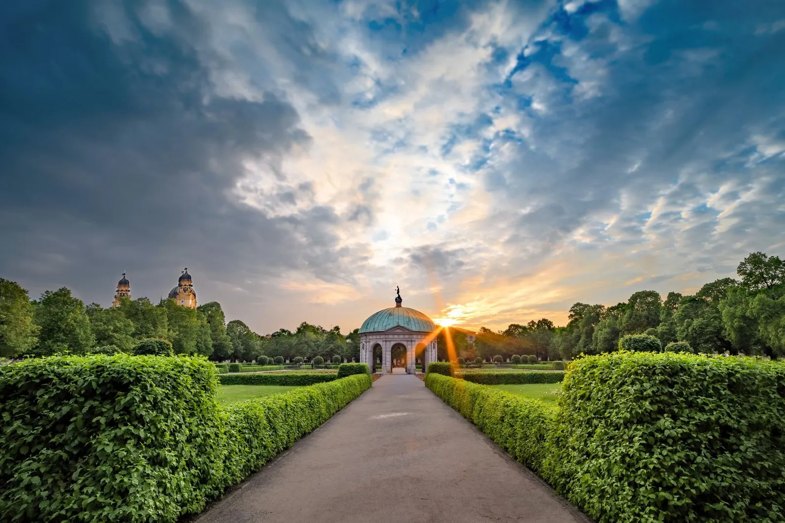 Pavillon de jardin au bout d'une allée bordée de haies, au coucher du soleil